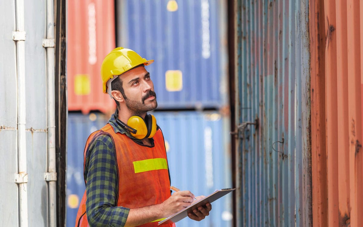shipping-transport-worker-communications-commskit Frontline worker at a shipyard signing a communications document in front on a shipping container